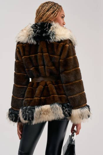 Person successful a luxurious fur overgarment with contrasting trims and glossy leather pants, holding a purse, seen from behind