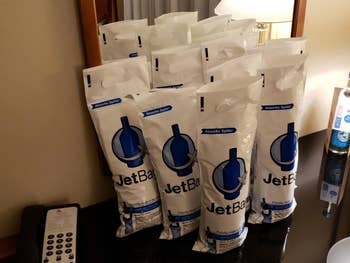 Eight JetBag wine transport bags are displayed on a hotel room table next to a phone, ideal for spill-free travel