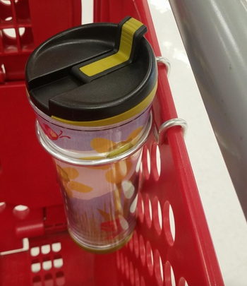 A reusable coffee cup in a metal holder attached to a Target cart 