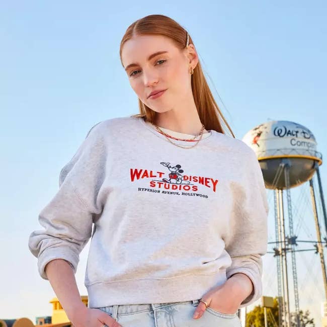 a model in a gray sweatshirt with walt disney studios logo embroidered on it