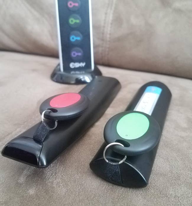 reviewer photo of the red and green trackers attached to two tv remotes, with the tracking remote in the background
