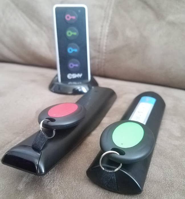 reviewer photo of the red and green trackers attached to two tv remotes, with the tracking remote in the background