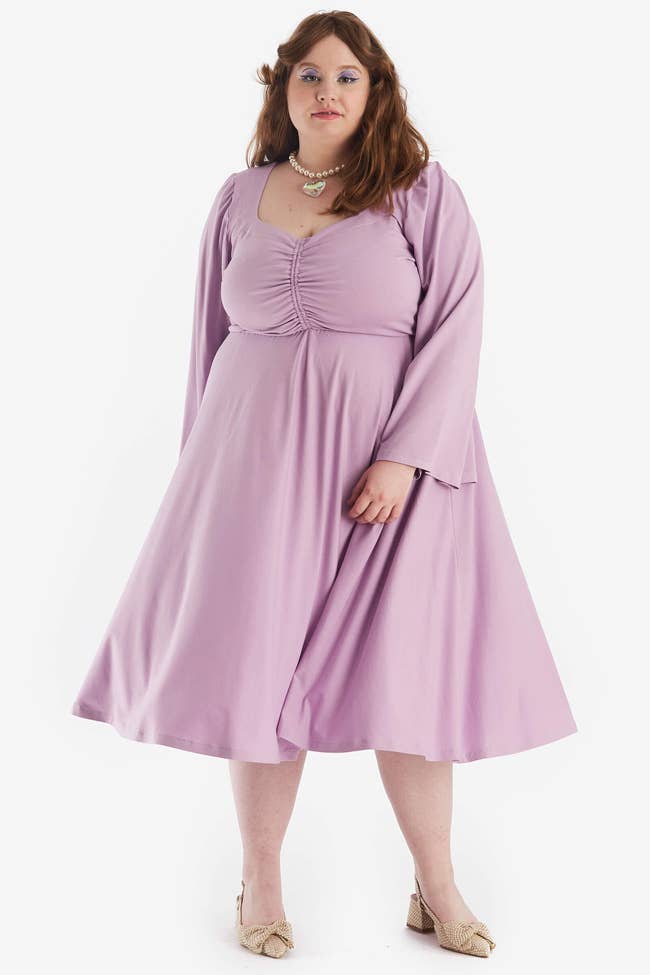 Model in a long flare sleeved purple midi dress with cinched chest detailing