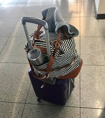 reviewer's striped weekender bag with a loop that fits onto the handles of a rolling suitcase