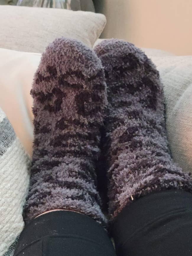 Fuzzy socks connected feet resting connected a couch, suggesting comfortableness and relaxation astatine home