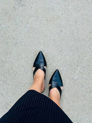 Person wearing stylish pointed-toe achromatic  flats with crisscross straps, paired with a pinstriped skirt