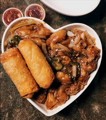 A heart-shaped plate filled with egg rolls and a chicken dish,
