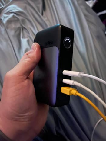 reviewer holding portable power bank with three connected charging cables