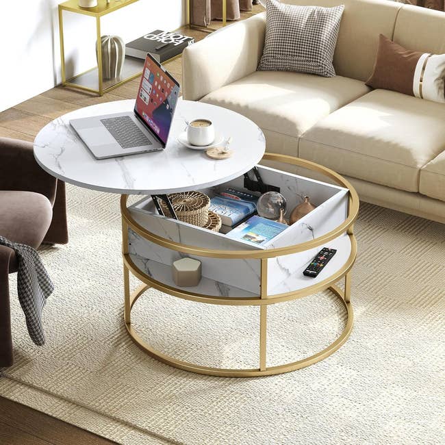 Round marble-top coffee table with gold accents and a lower shelf containing books and decorative items