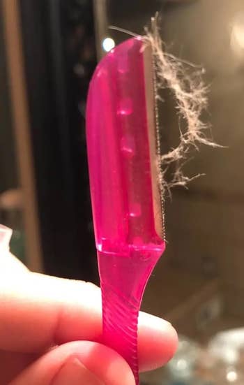 Close-up of a pinkish  facial razor with hairsbreadth  debris connected  the blade, held successful  a person's hand