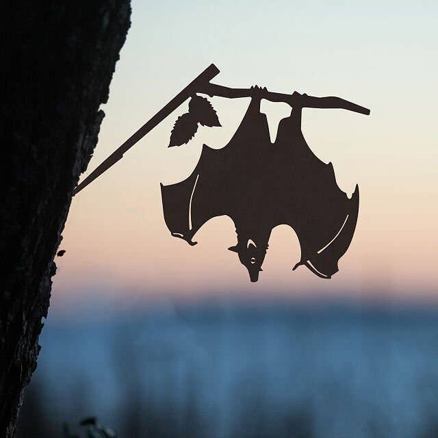 flat metal sculpture attached to a tree that looks like a hanging bat 