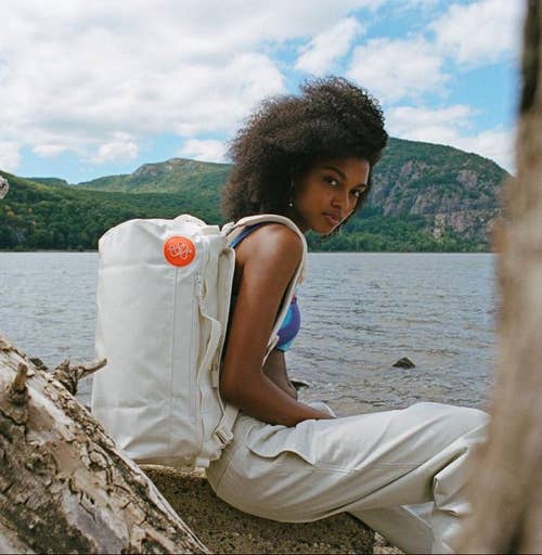 Model with the mini to-go bag on their back worn as a backpack in cream color against a nature background