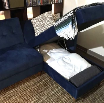 reviewer photo of navy blue couch, opening up for storage space