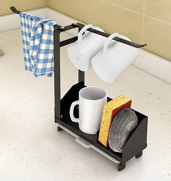 caddy on a counter holding sponges, towel, and small mugs, with arms turned in opposite directions