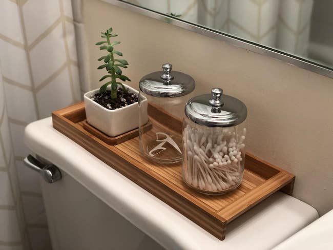 reviewer's shallow bamboo tray on top of toilet holding a succulent and two jars