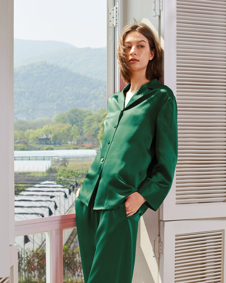 model wearing longsleeve forest green silk pajamas, leaning on a balcony overlooking a greenhouse