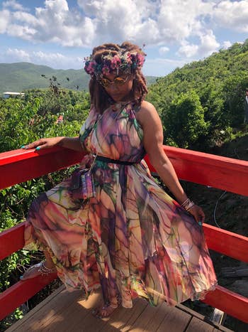 reviewer in a floral dress and headpiece sitting on a red bridge railing, outdoors