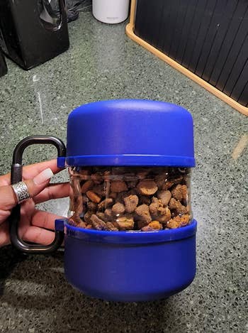 Hand holding a portable blue pet treat container with a clip. Perfect for pet owners on the go