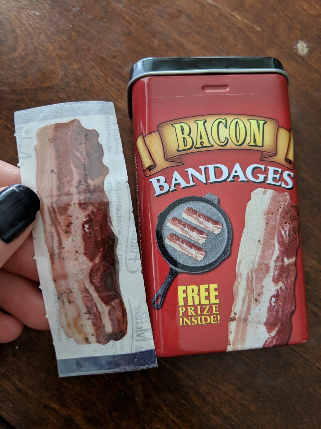 image of reviewer's hand holding a bacon bandage in front of the tin of bandages