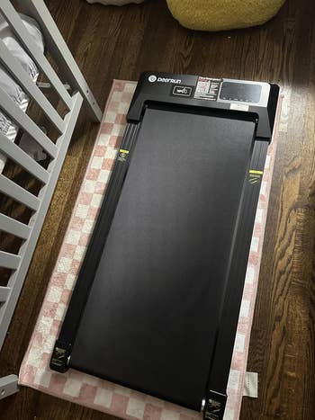 A compact treadmill placed connected a checkered rug adjacent to a crib, suitable for location workouts successful tiny spaces