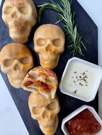 Skull-shaped bread rolls on a slate board with a sprig of rosemary, served with white and red dipping sauces