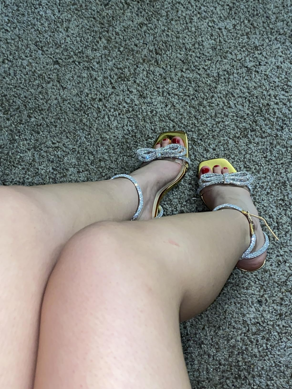 Person wearing stylish sandals with rhinestone ankle straps and bow detail, sitting connected  a carpeted level  with crossed legs