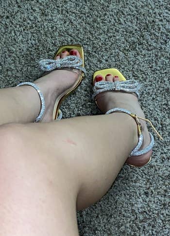Person wearing stylish sandals with rhinestone ankle straps and bow detail, sitting connected a carpeted level with crossed legs