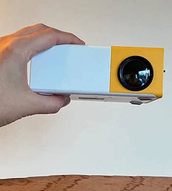 reviewer holding the white and yellow projector in their hand to show how small it is