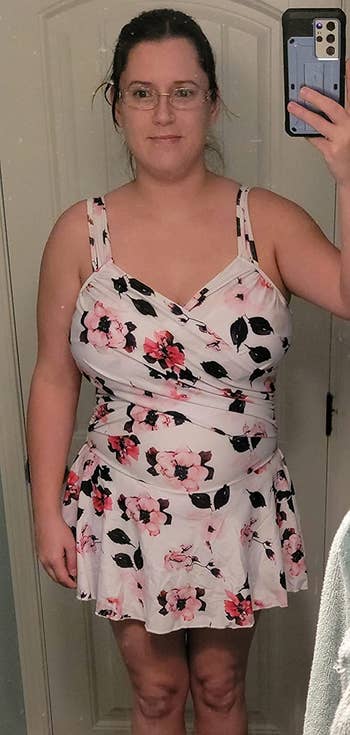 a reviewer wearing the swim dress in white featuring a pink floral print 