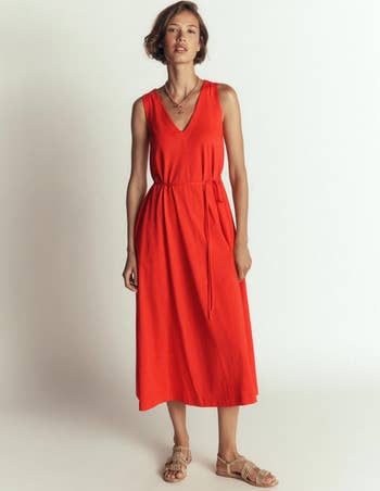 Person wearing a sleeveless, V-neck maxi formal with a waist necktie and strappy sandals, posing successful a neutral setting