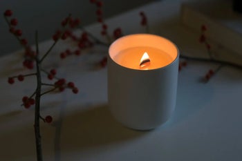 a lit wood wick candle in a white ceramic jar