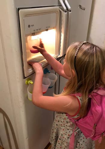 a reviewer's child using the cups to get water from a fridge door dispenser 