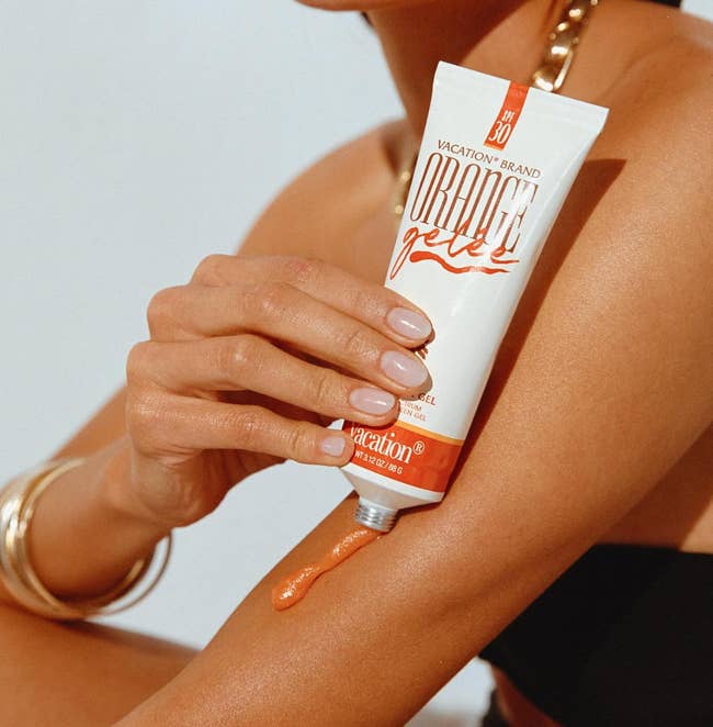 Person applying Vacation marque  SPF 30 gel connected  their arm, showcasing skincare successful  summertime  weather. They deterioration  a achromatic  apical  and golden  bangles