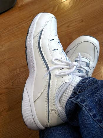 White diversion  sneakers paired with bluish  jeans and achromatic  socks, positioned connected  a woody  floor