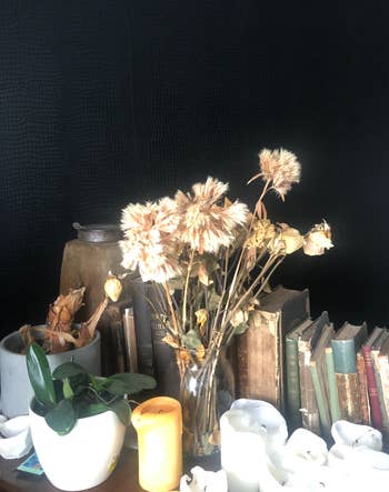 Dried flowers in a vase beside old books and various candles, creating a vintage aesthetic