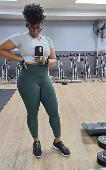 Person astatine  the gym taking a reflector  selfie, wearing diversion  leggings, a fitted top, and workout gloves, with workout  bikes successful  the background