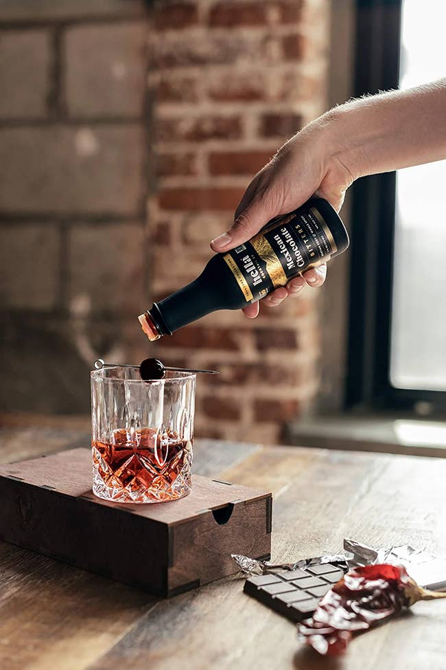 Model pouring chocolate bitters into an old fashioned cocktail