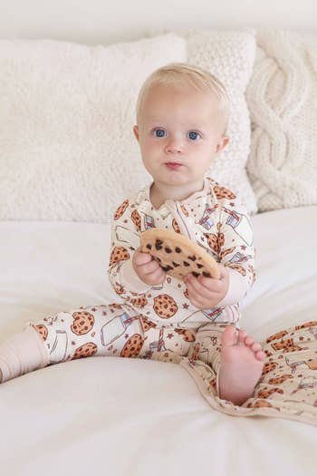 Baby successful  cookie-patterned pajamas holds a ample  cooky  portion    sitting connected  a bed, showcasing cozy loungewear for kids