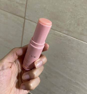 Hand holding a pinkish articulator balm against a neutral tiled background