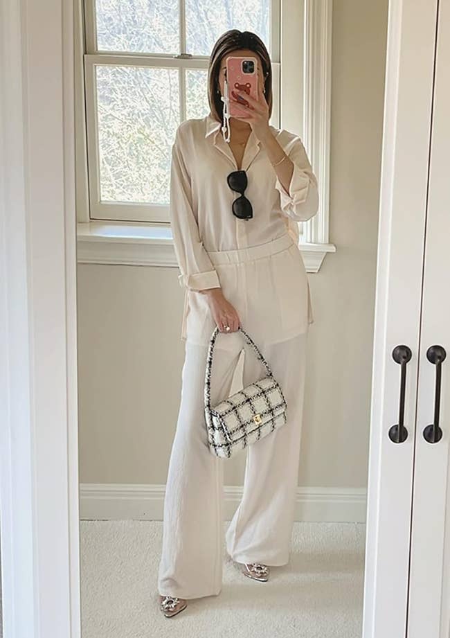 Person taking a reflector selfie successful a chic, loose-fitting outfit with sunglasses connected the shirt, holding a patterned handbag