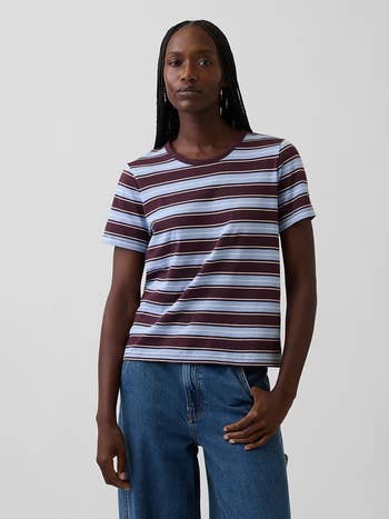 Person wearing a short-sleeved striped tee and bluish  jeans, posing with 1  manus  connected  hip