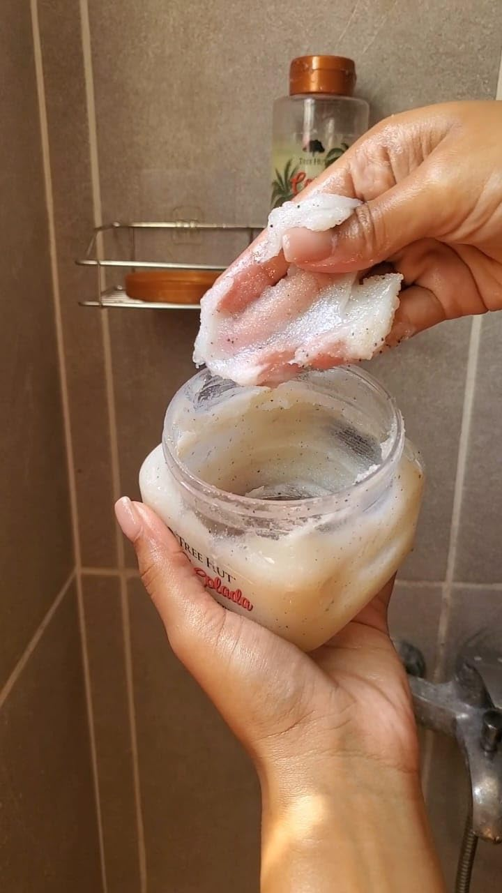 Person holding body scrub container, scooping product with fingers in a bathroom setting