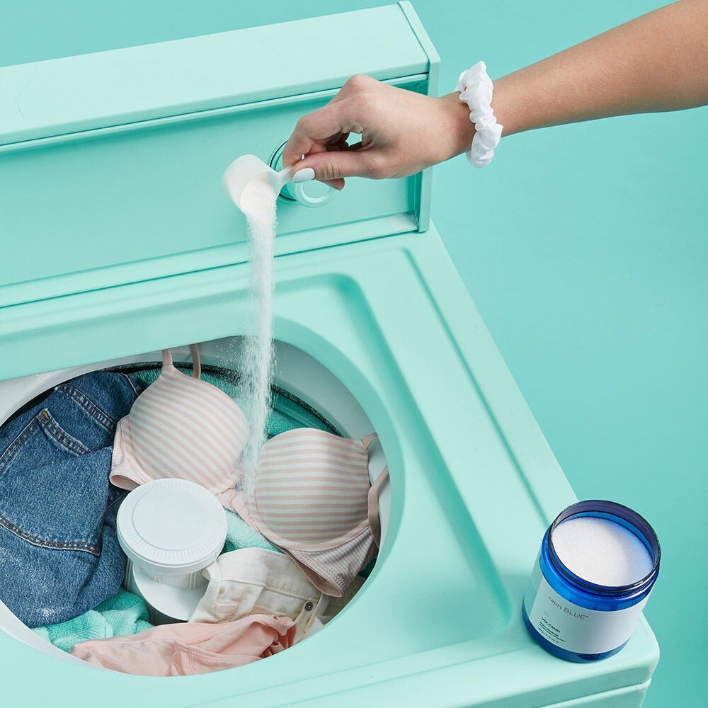 model pouring a bit of the scent booster into their laundry