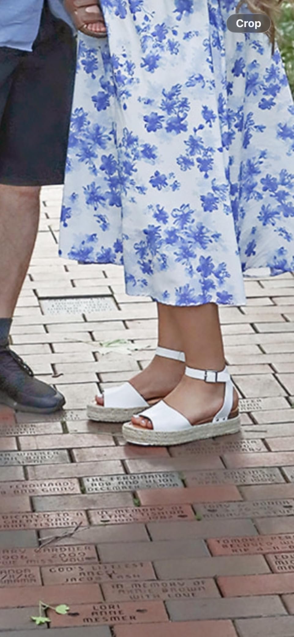 Person wearing floral formal  and espadrille sandals stands adjacent  to idiosyncratic    successful  shorts and shoes connected  a walkway with engraved bricks
