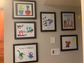 A reviewer's gallery wall of kids' art in black frames