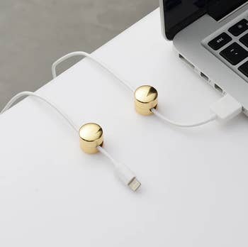 the little cord holders in gold attached to desk holding up chargers