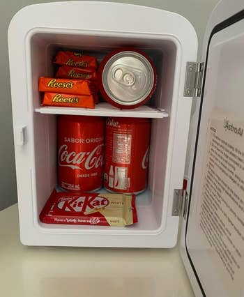 reviewer photo of the inside of the mini fridge holding cans of soda and candy