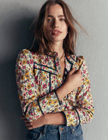 Person wearing a floral blouse with puffed sleeves and jeans, lasting against a plain backdrop, manus resting connected shoulder