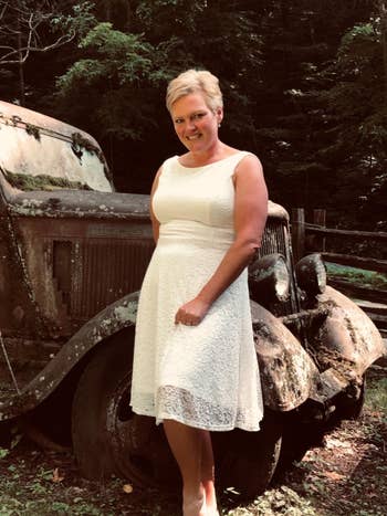 Reviewer standing in front of rusted black Jeep and knee-high white sleeveless lace dress with a boat neckline 