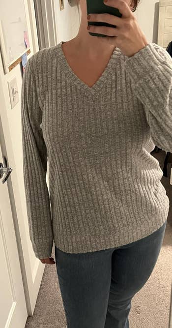 Person taking a reflector  selfie, wearing a ribbed V-neck sweater and jeans, capturing a casual outfit